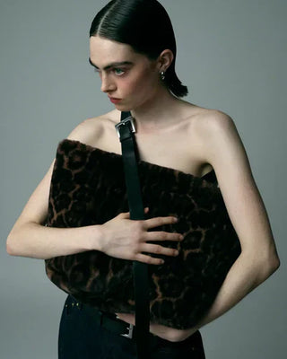 Model with black hair holds marble-patterned brown fur piece across chest, wearing black pants with leather belt against grey backdrop.